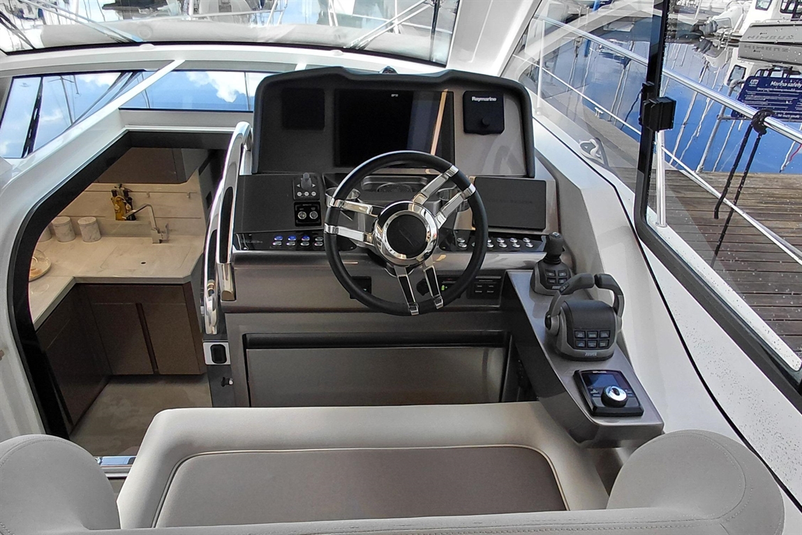 Modern yacht interior showing the steering wheel, control panel, and kitchenette with a sink and marble countertop.